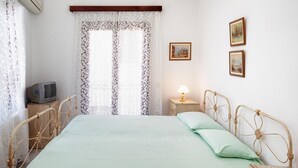 Ein Zimmer mit einem Bett, einem Nachttisch, einer Lampe, einem Fernseher und zwei gerahmten Bildern an der Wand.
