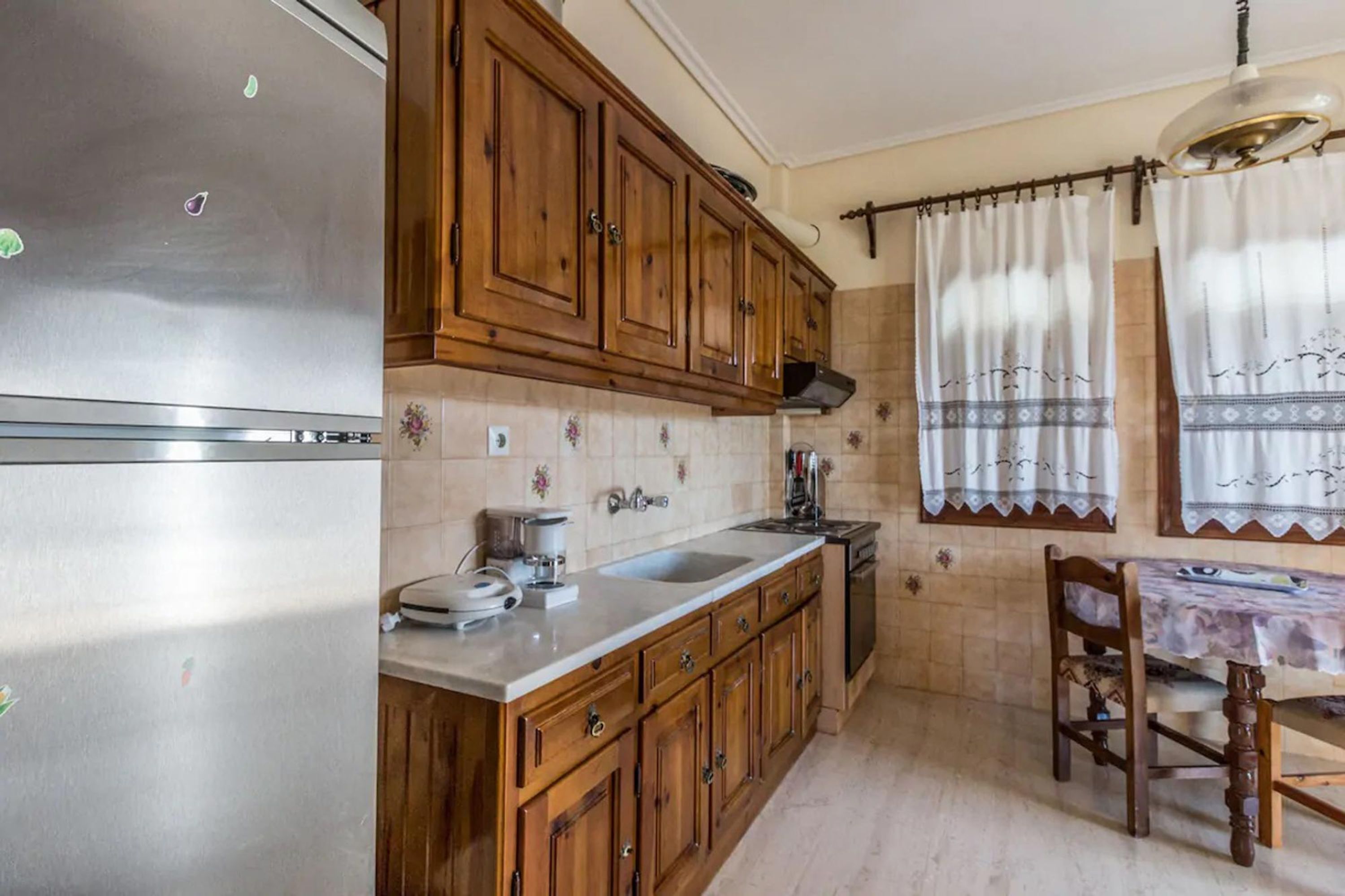 Een keuken met houten kastjes, een roestvrijstalen koelkast, een spoelbak en een eettafel met stoelen.