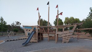 Una struttura gioco a forma di nave pirata in legno, con scivolo e rete da arrampicata.
