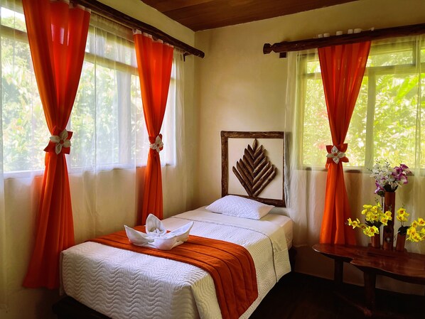 Un dormitorio con una cama, cortinas naranjas, cabecero de madera y un jarrón con flores.