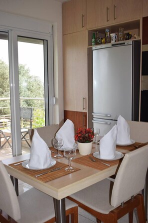 Un coin repas avec une table dressée pour deux personnes, un réfrigérateur et une vue sur l’extérieur.