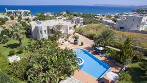 Ein modernes Resort mit einem zentral gelegenen Schwimmbad, umgeben von üppiger Vegetation und Palmen, mit Blick auf die Küste.