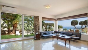 Ein geräumiges Wohnzimmer mit großen Schiebeglastüren zum Garten, einer Sofagarnitur, einem Couchtisch und Blick auf das Meer.