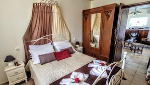Een opgemaakt bed met hemeltje, een houten garderobe en een klein nachtkastje met een lamp.