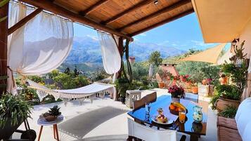 Un espace extérieur aménagé, abrité et doté de tables préparées pour le petit-déjeuner, entouré de plantes en pot et offrant une vue sur les montagnes.