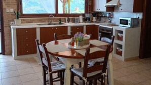 Een keuken met een centraal eiland, houten kastjes, een eettafel met stoelen en een groot raam met uitzicht.