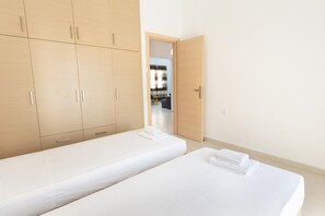 A room with two single beds, a wooden wardrobe, and a door leading to a living area. - Mirsini's Apartment in Chania center (Chania)