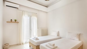 Et rent, moderne hotelværelse med to enkeltsenge, et lille vindue med lette gardiner, en radiator og en vægmonteret hylde med planter.