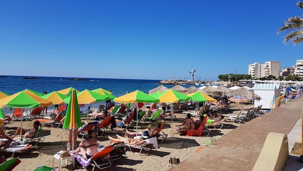 En strand med rækker af farverige parasoller og liggestole.
