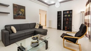 En moderne stue med en grå hjørnesofa, et glasbord, en sort lænestol og et billede på væggen.