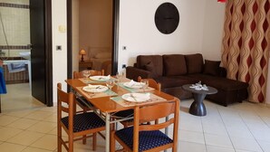 A dining area with a table set for two, a sofa, and a clock on the wall. - Ilia's Apt in Chania (Chania)