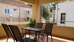 A balcony with a glass table and four chairs, overlooking a residential area with tiled roofs and white walls. - Ilia's Apt in Chania (Chania)