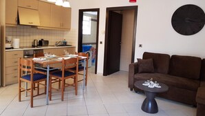 A modern kitchen with wooden cabinets and a dining area with a table and chairs. There is a brown sofa and a small round table in the living area. - Ilia's Apt in Chania (Chania)