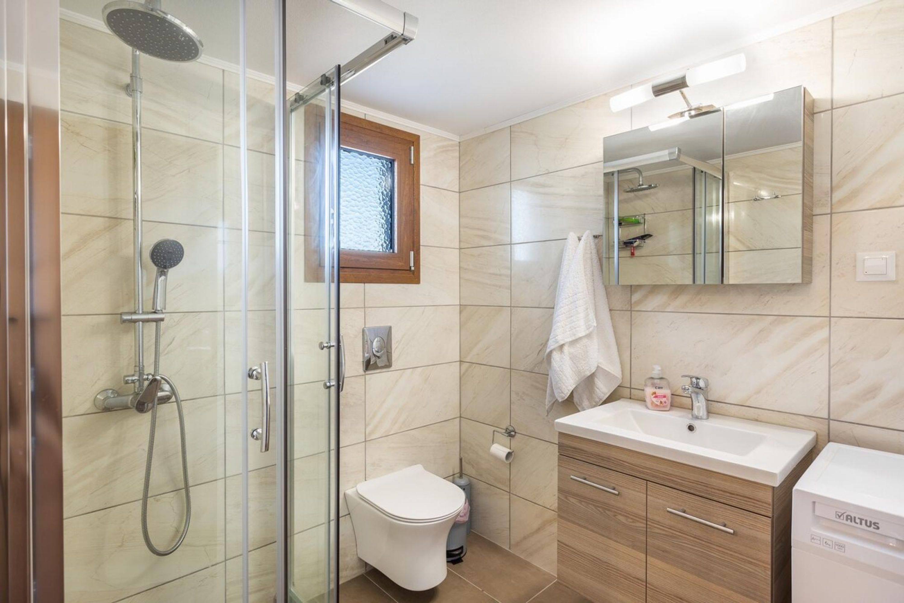 A modern bathroom with a glass-enclosed shower, a toilet, a sink with a mirror, and a window.
