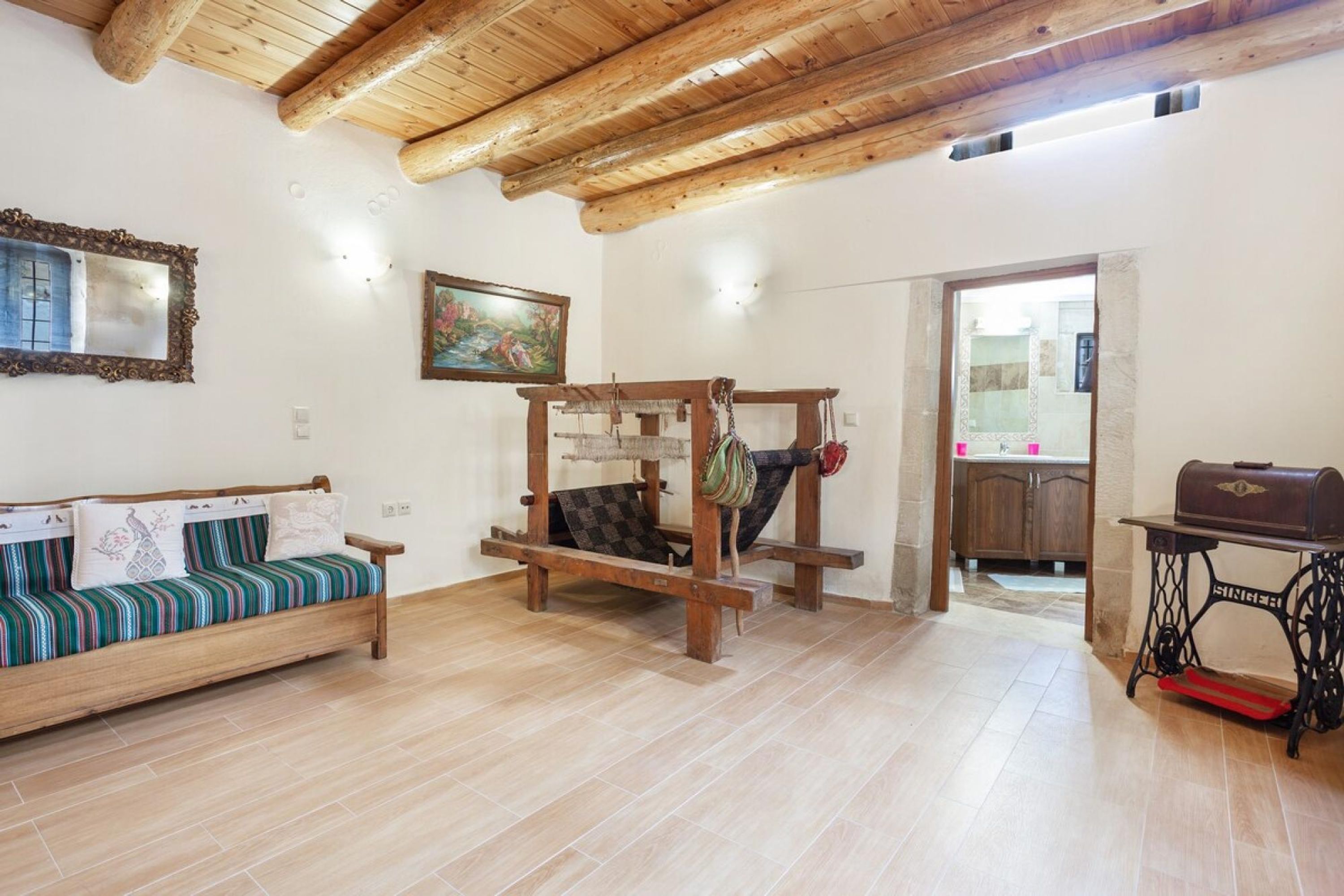 Een kamer met een houten plafond, een bank met gestreepte kussens, een houten tafel en een naaimachine.