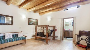 A room with a wooden ceiling, a sofa with striped cushions, a wooden table, and a sewing machine. - Traditional Stone House Rafael (Tzitzifes)