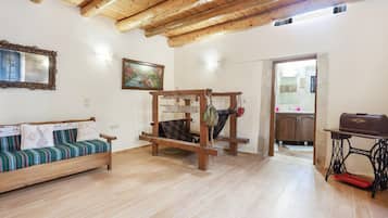 Een kamer met een houten plafond, een bank met gestreepte kussens, een houten tafel en een naaimachine.