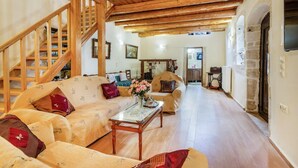 A cozy living room with a wooden staircase, a sofa set, a coffee table, and a television. - Traditional Stone House Rafael (Tzitzifes)