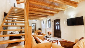 A spacious living area with a wooden staircase, comfortable seating, and a flat-screen TV mounted on the wall. - Traditional Stone House Rafael (Tzitzifes)