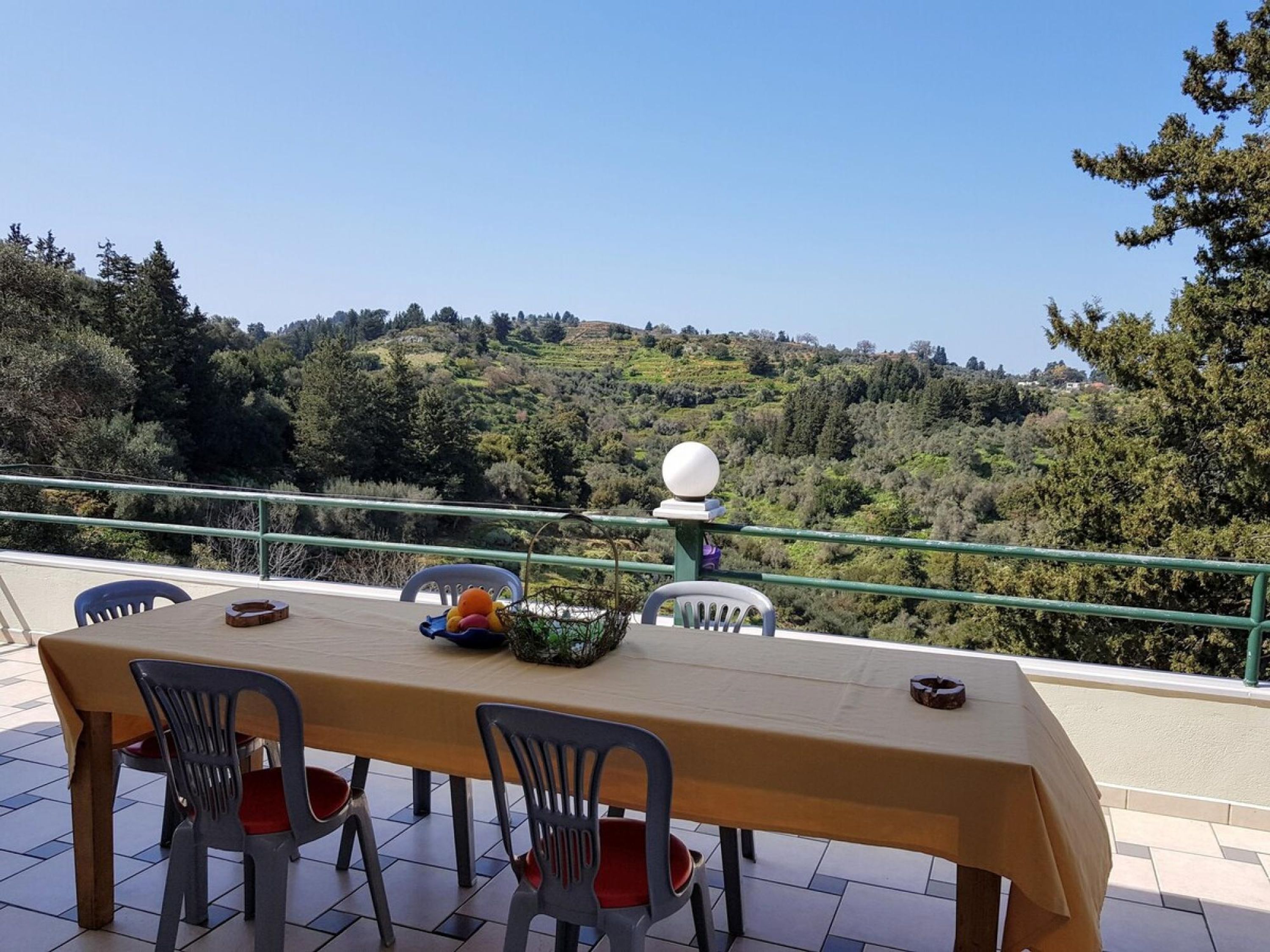 Een terras met een tafel en stoelen, een decoratieve schaal, en uitzicht op een glooiend landschap.