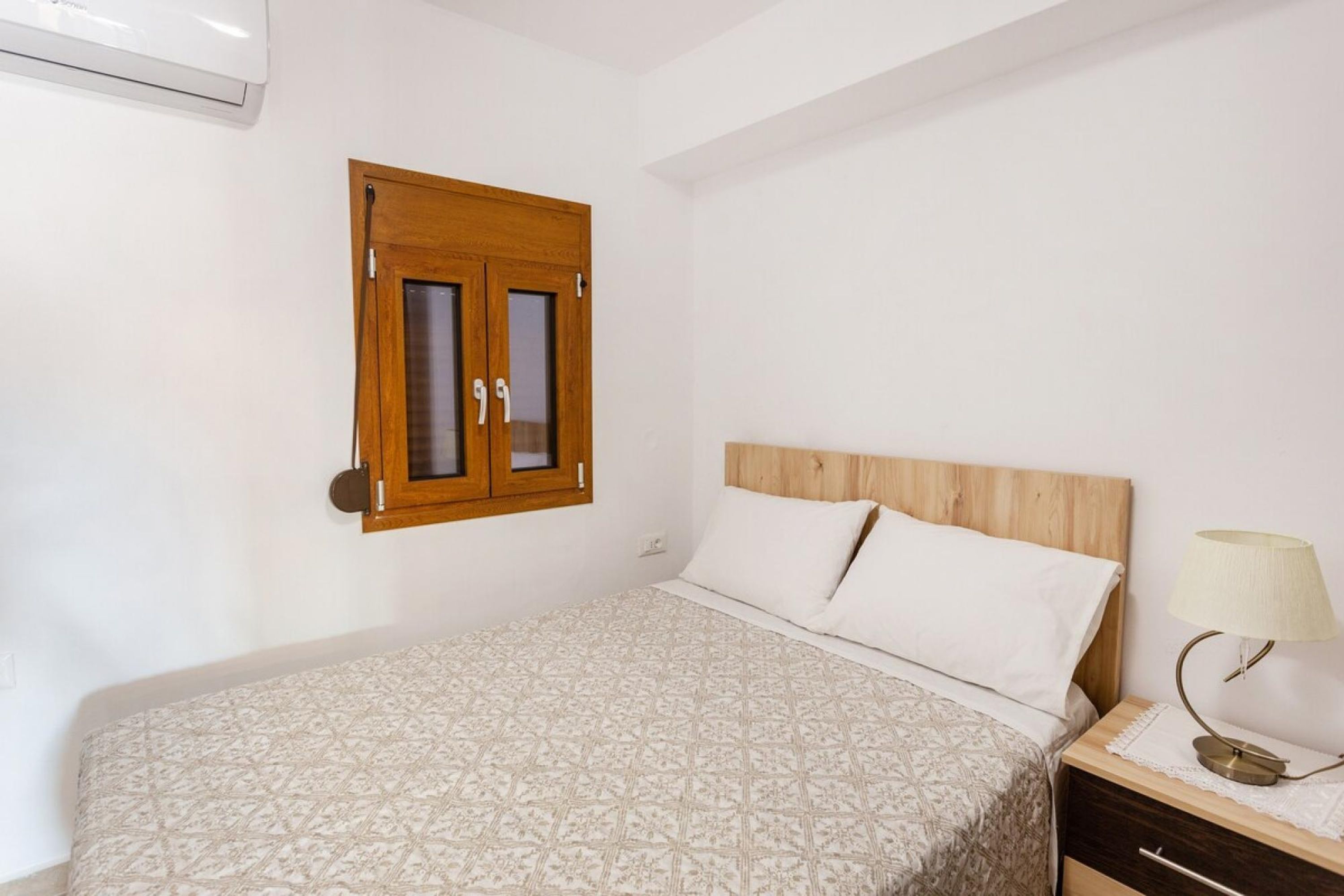 Une chambre à coucher avec un lit, une tête de lit en bois, une table de chevet avec une lampe et une porte en bois dotée de panneaux de verre.