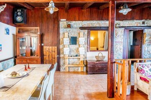 Un'atmosfera rustica con pareti in legno, un camino in pietra, un'area pranzo con tavolo in marmo e un angolo salotto accogliente con cuscini decorati.