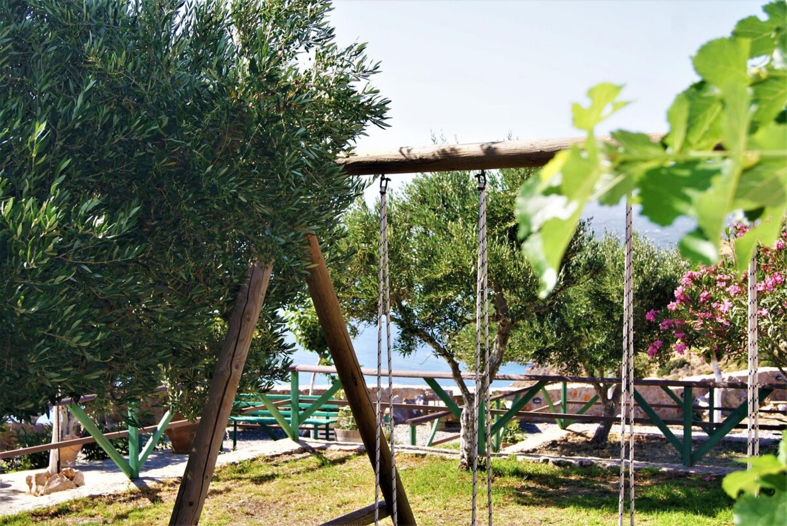 A wooden swing set in a park with green benches and trees.