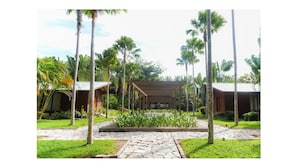 Un complexe hôtelier comprenant plusieurs chalets en bois, une allée couverte centrale et une végétation tropicale luxuriante.