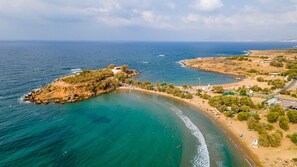 Vista aérea de una zona costera con playa, afloramientos rocosos y un pequeño poblado con edificios y vegetación.