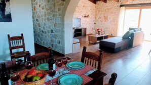 A cozy dining area with a stone wall, wooden ceiling, and a dining table set with plates, glasses, and a fruit basket. - Traditional Villa in Pemonia (Pemonia)