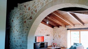 A stone-walled room with a wooden ceiling, a television, a sofa, and a small table with a vase. - Traditional Villa in Pemonia (Pemonia)