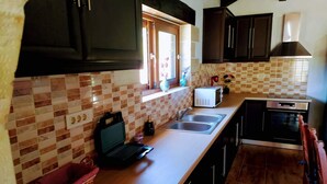 A kitchen with dark cabinets, a microwave, a toaster, a sink, and a window with decorative items. - Traditional Villa in Pemonia (Pemonia)