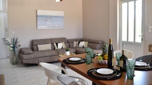 Un comedor con una mesa de madera preparada para dos personas, un sofá al fondo y un cuadro en la pared.