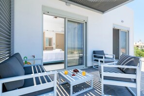 A balcony with white furniture, a glass door leading to a room, and a table with fruits and juice. - Villa Kalliopi - Agios Onoufrios (Kounoupidiana)