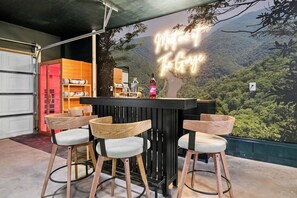 Eine Bar mit Neonreklame, Holzsesseln und Blick auf eine bewaldete Landschaft.