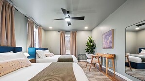 Ein Hotelzimmer mit zwei Betten, einem Schreibtisch, einem Stuhl, einem Deckenventilator und einem großen Spiegel.