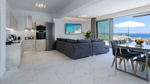 A modern living space with a kitchen, dining area, and a large window offering a view of the sea. - Villa Erato – Agios  Onoufrios (Kounoupidiana)