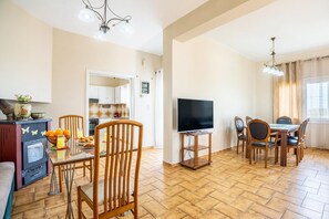 A dining area with a TV, wooden chairs, and a table. - Ortansia House  near the Sea (Maleme)