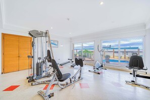 A gym with various exercise machines, a wooden door, and large windows offering a view of the outdoors.