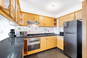A modern kitchen with wooden cabinets, a stainless steel refrigerator, a gas stove, and a built-in oven.