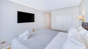 A bedroom with a bed, a TV mounted on the wall, a radiator, and a wardrobe. - Rincón Almar 2D, Wifi & Estacionamiento (Viña del Mar)