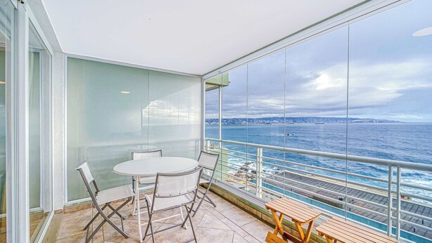 A balcony with a table and chairs, overlooking a body of water with a view of the coastline. - Rincón Almar 2D, Wifi & Estacionamiento (Viña del Mar)
