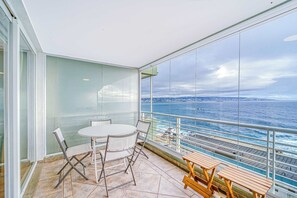 Een balkon met een tafel en stoelen, met uitzicht op een waterpartij en de kustlijn.