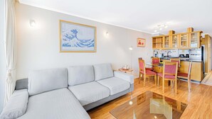 A modern living room with a sofa, dining table, chairs, and a kitchen area with wooden cabinets and appliances. - Rincón Almar 2D, Wifi & Estacionamiento (Viña del Mar)