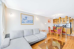 A modern living room with a sofa, dining table, chairs, and a kitchen area with wooden cabinets and appliances.