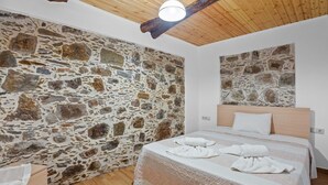 A bedroom with a stone wall, a wooden ceiling, and a bed with white linens. - Maria's House with View in Kambos (Kampos)