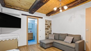 A cozy room with a wooden ceiling, a grey sofa, a flat-screen TV, and a stone wall. - Maria's House with View in Kambos (Kampos)