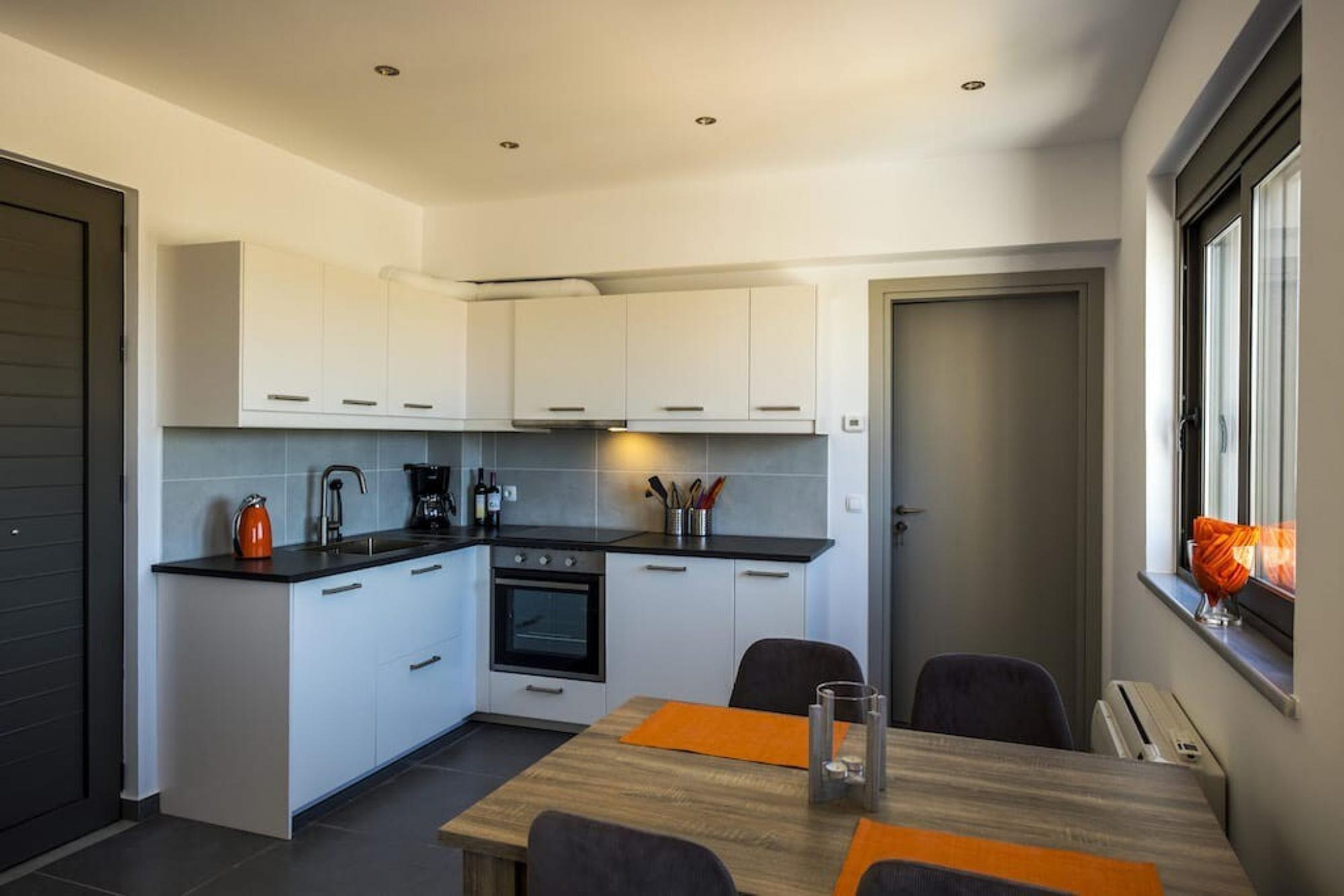 A compact kitchen with white cabinets, a black countertop, and a dining area with a table and chairs.