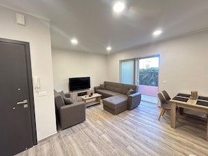 Ein modernes Wohnzimmer mit Flachbildfernseher, einer Couch, einem Couchtisch und einer Essecke mit Tisch und Stühlen.