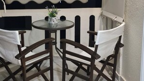 Un espace extérieur abrité, aménagé avec une table ronde et deux chaises, une petite plante en pot posée sur la table et un tapis noir sur le sol.